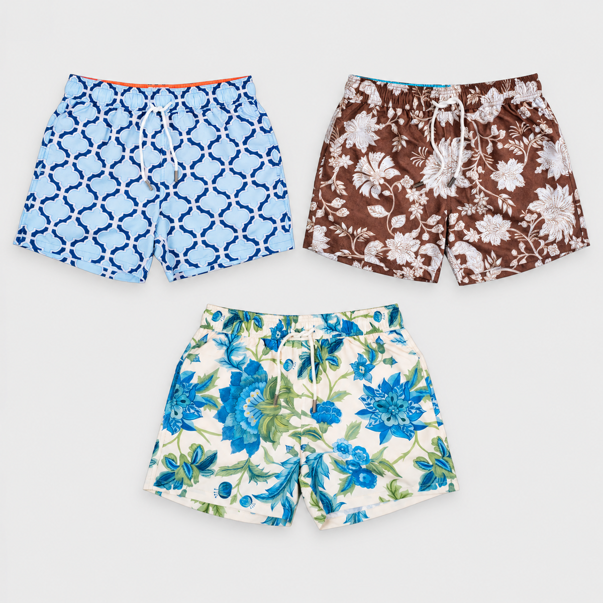 Three MARONI swim shorts in blue geometric, brown floral and blue floral prints, arranged as a flat lay